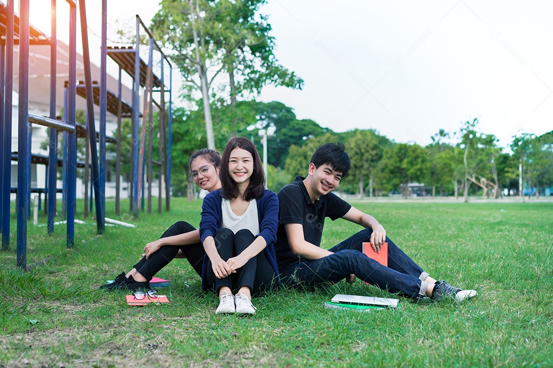 Grupo de jovens estudantes asiáticos com pastas escolares na grama na faculdade