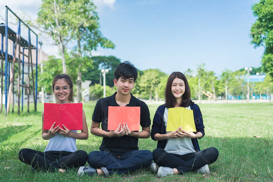 Grupo de jovens estudantes sentado sorrindo na grama com pastas escolares
