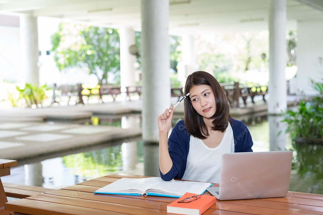 Aluna sorrindo escrevendo com livro de pastas escolares e laptop na Universidade