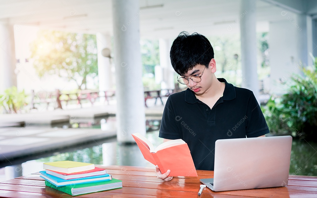 Jovem lendo pasta de livro escolar com computador portátil