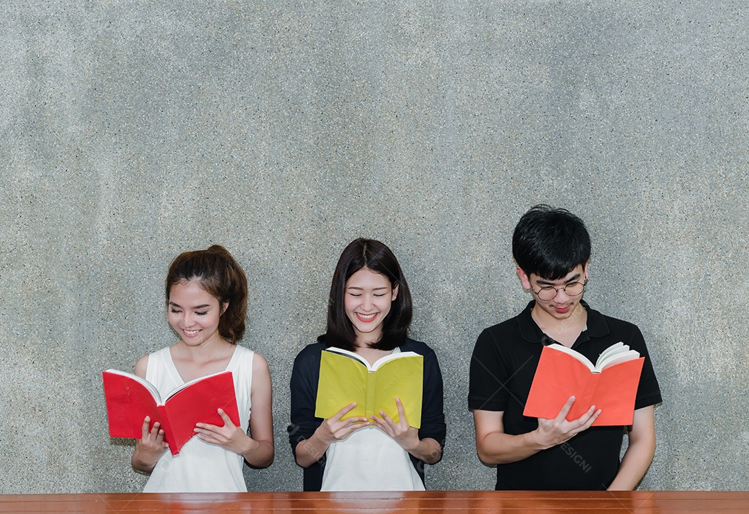 Jovens estudantes asiáticos juntos sorriem em grupo com pastas escolares lendo livro