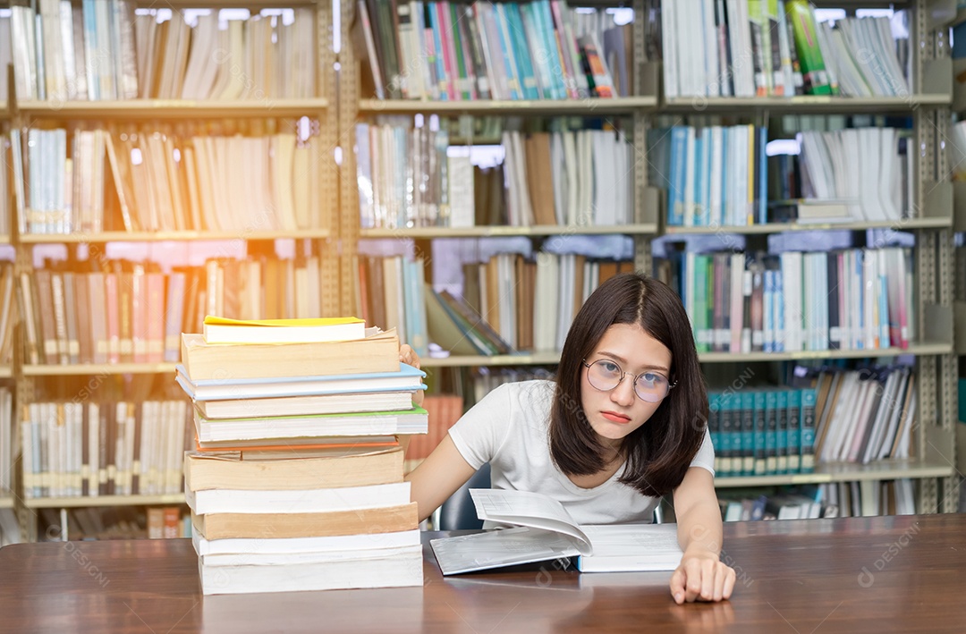 Jovem asiática com óculos seriamente e lendo livro na biblioteca