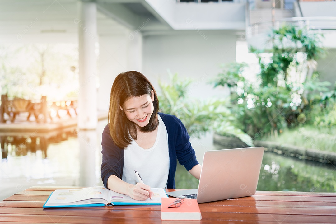 Jovem estudante escrevendo sério com livro de pastas escolares e laptop