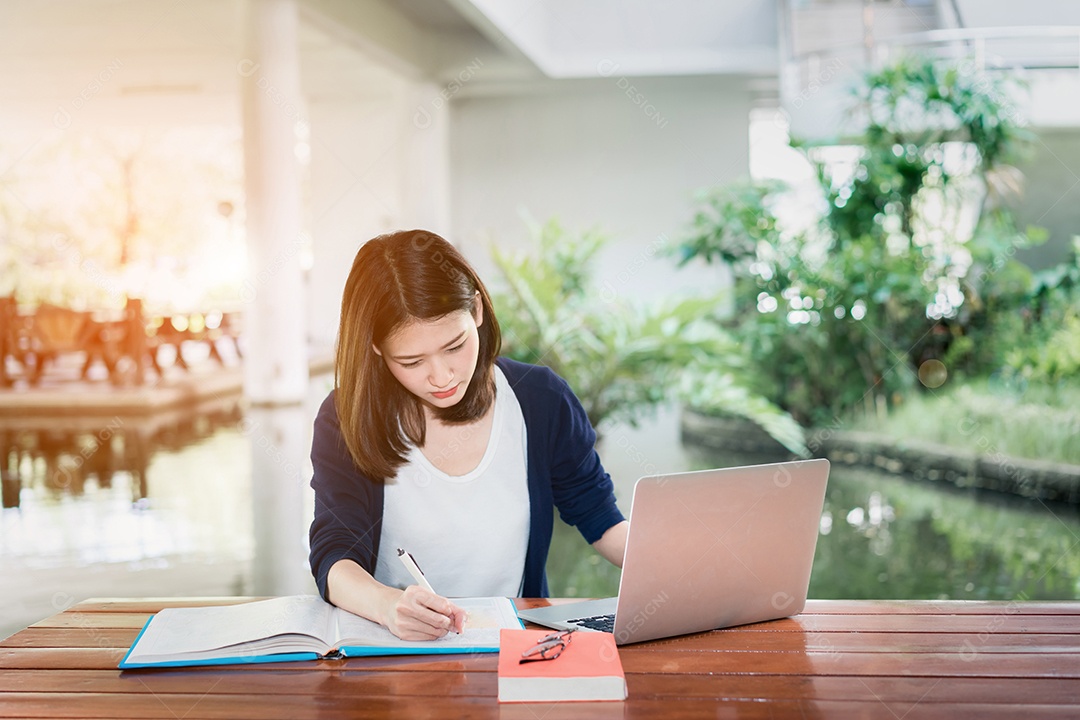 Jovem estudante escrevendo sério com livro de pastas escolares e laptop