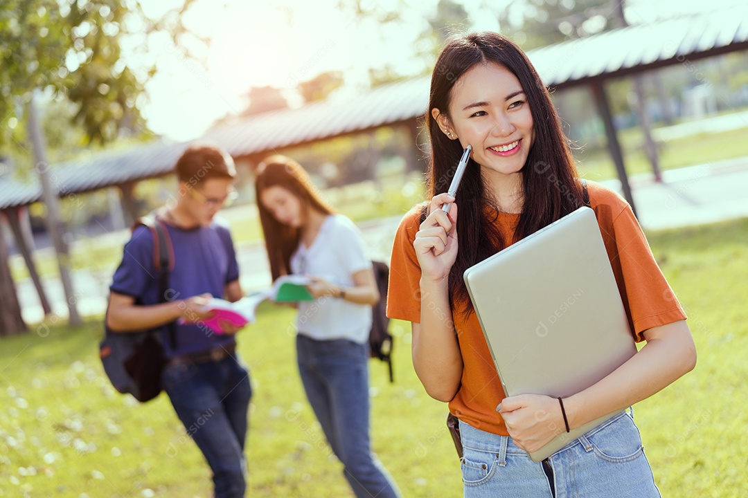Estudantes asiáticos juntos sorrindo estudo de livro de leitura em grupo com laptop no campus da escola