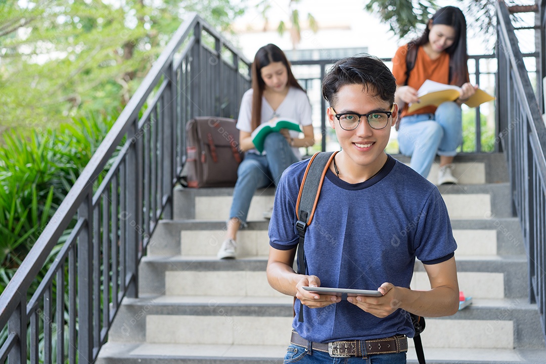 Estudantes jovens asiáticos juntos lendo estudo de livro sorrindo com tablet no campus da escola