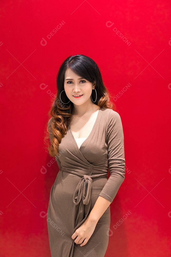 Linda jovem asiática com vestido de moda marrom luxo posando no estúdio de fundo vermelho
