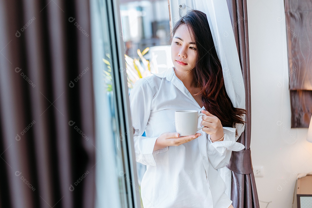 Mulher asiática acorda de manhã e abre a janela depois de acordar