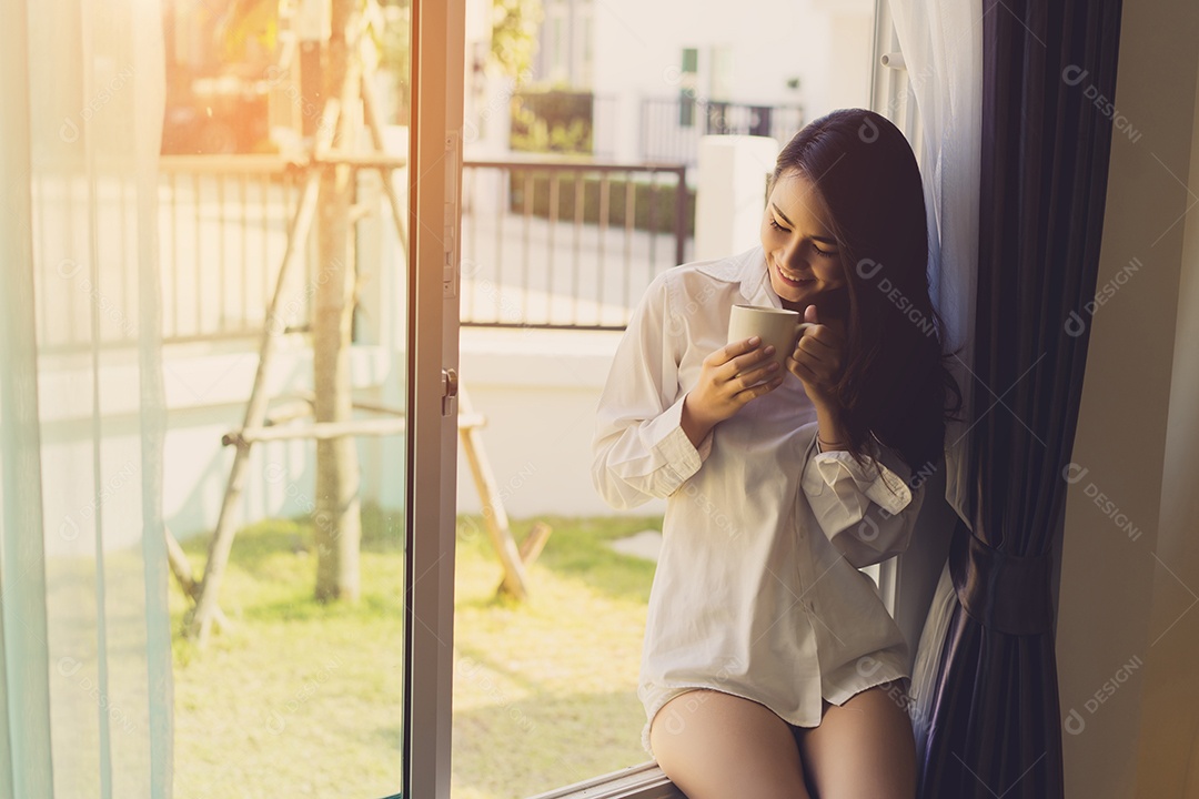 Mulher asiática tomando café da manhã na janela do quarto