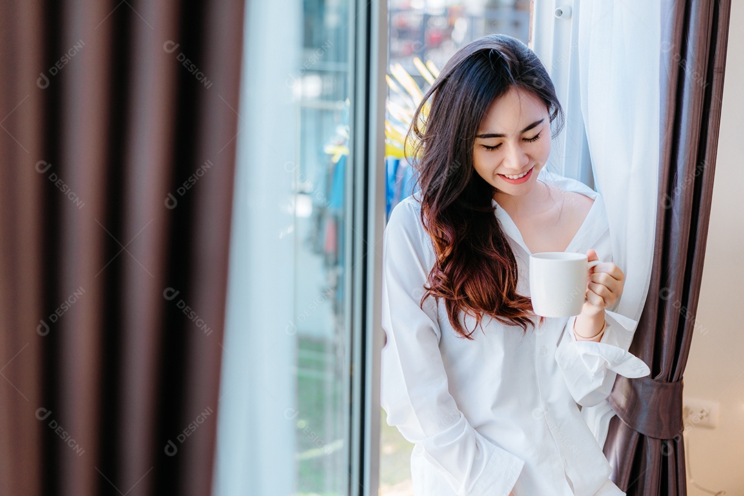 Mulher asiática tomando café da manhã na janela do quarto