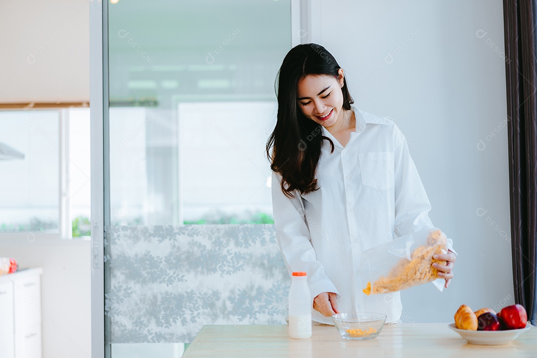 Mulher asiática comendo flocos de milho sorri na hora da manhã