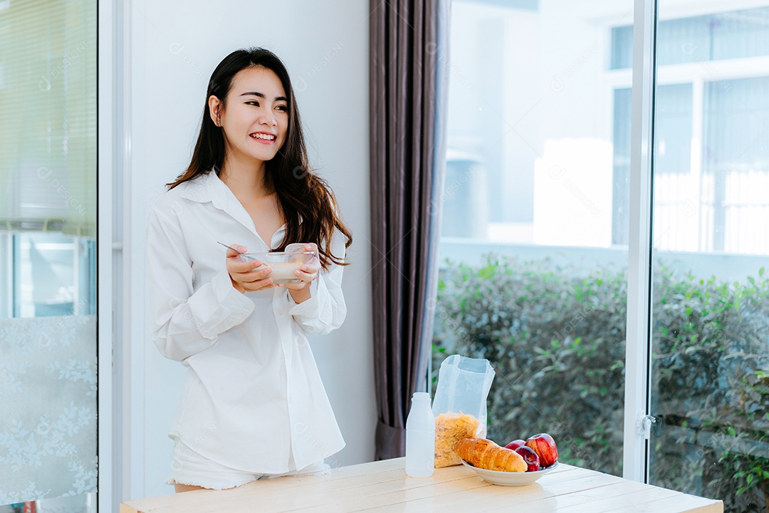 Mulher asiática comendo flocos de milho sorri na hora da manhã