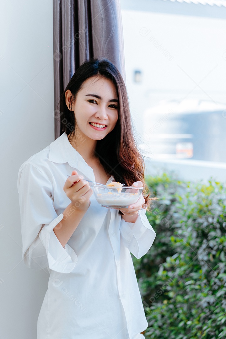 Mulher asiática comendo flocos de milho sorri na hora da manhã
