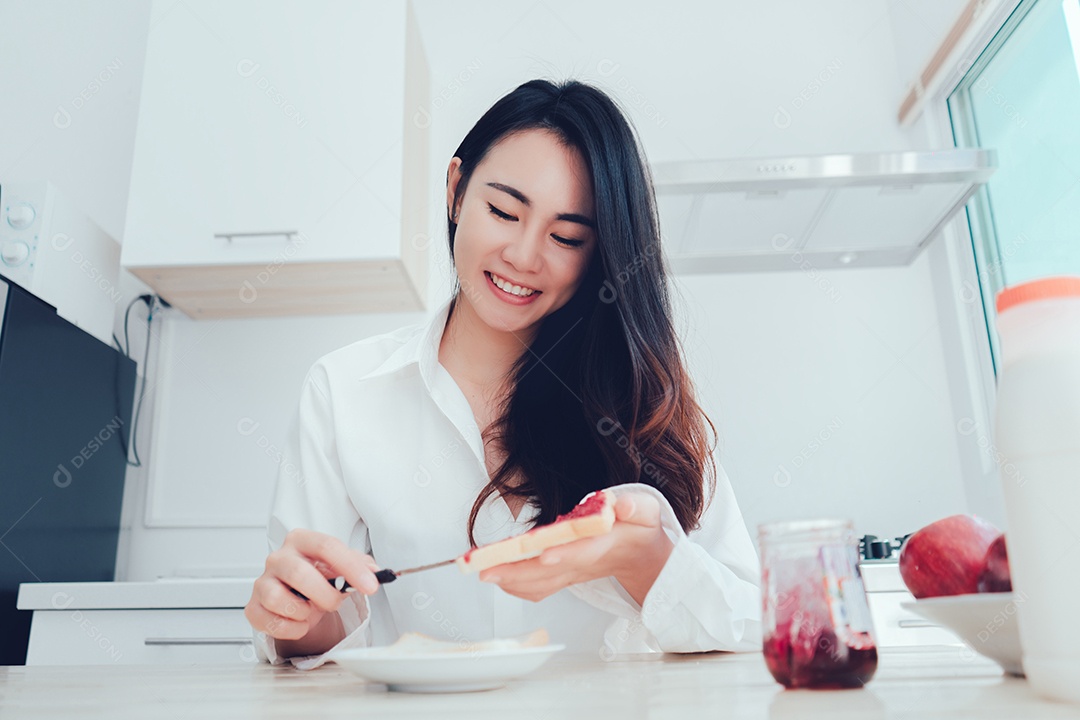 Mulher asiática fatia pão de geleia pela manhã e come frutas de maçã, café, comida saudável