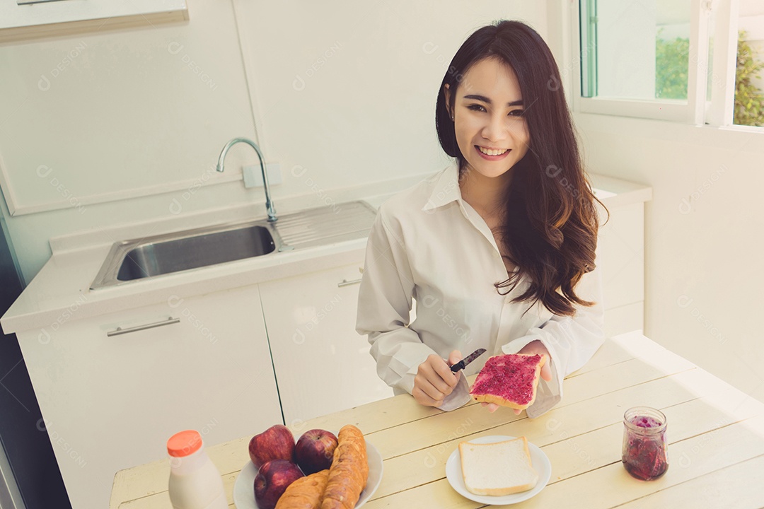Mulher asiática fatia pão de geleia pela manhã e come frutas de maçã, café, comida saudável