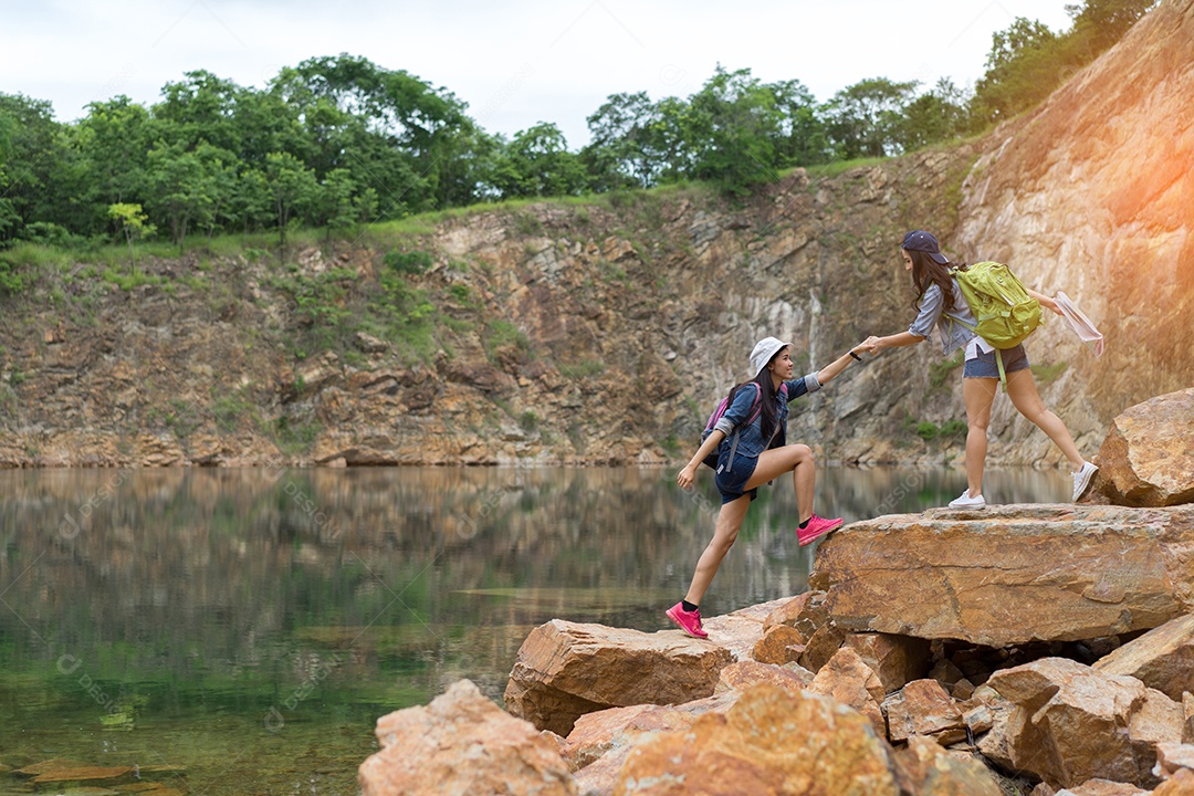 Jovens asiáticas ajudam amigas caminhando juntas com a mochila segurando a mão escalando