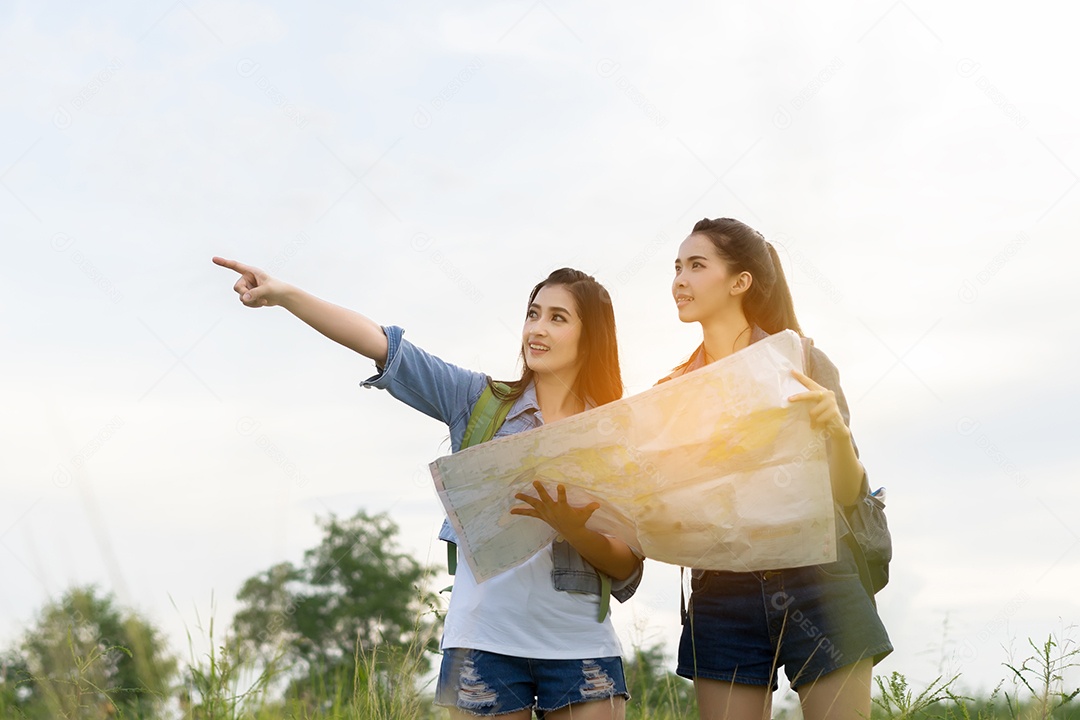 Menina asiática e amiga com mochila, mapas abertos, localização viagem na floresta