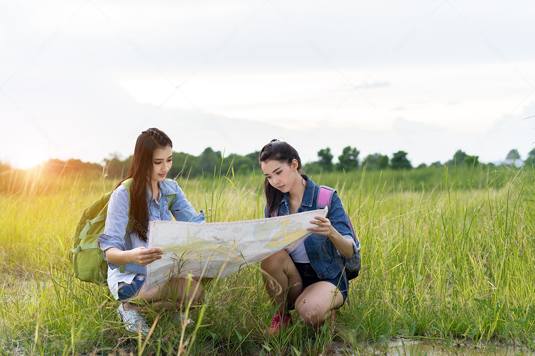 Menina asiática e amiga com mochila, mapas abertos, localização viagem na floresta