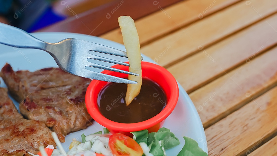 Batata frita em molho sobre mesa de madeira