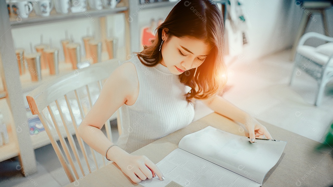 Menina asiática lendo livro de moda sentada na cafeteria