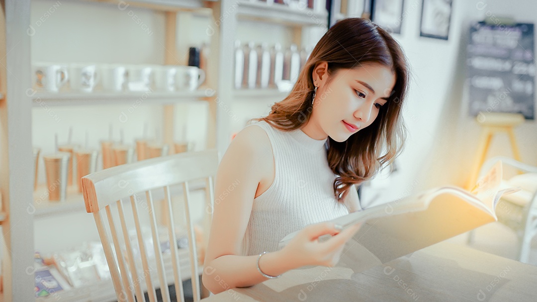 Menina asiática lendo livro de moda sorria na cafeteria