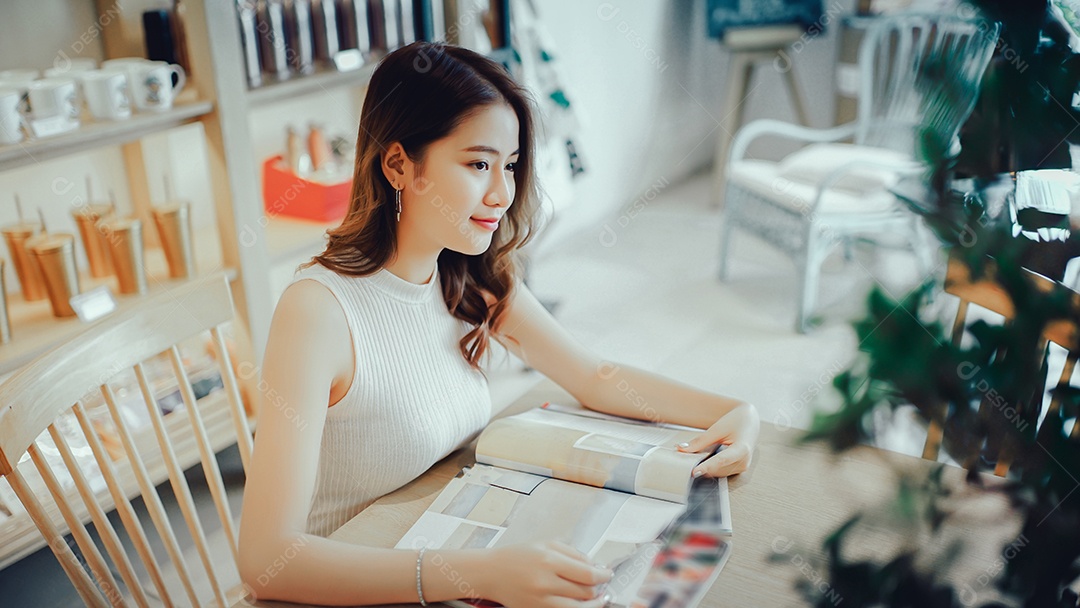 Menina asiática lendo livro de moda sorria na cafeteria