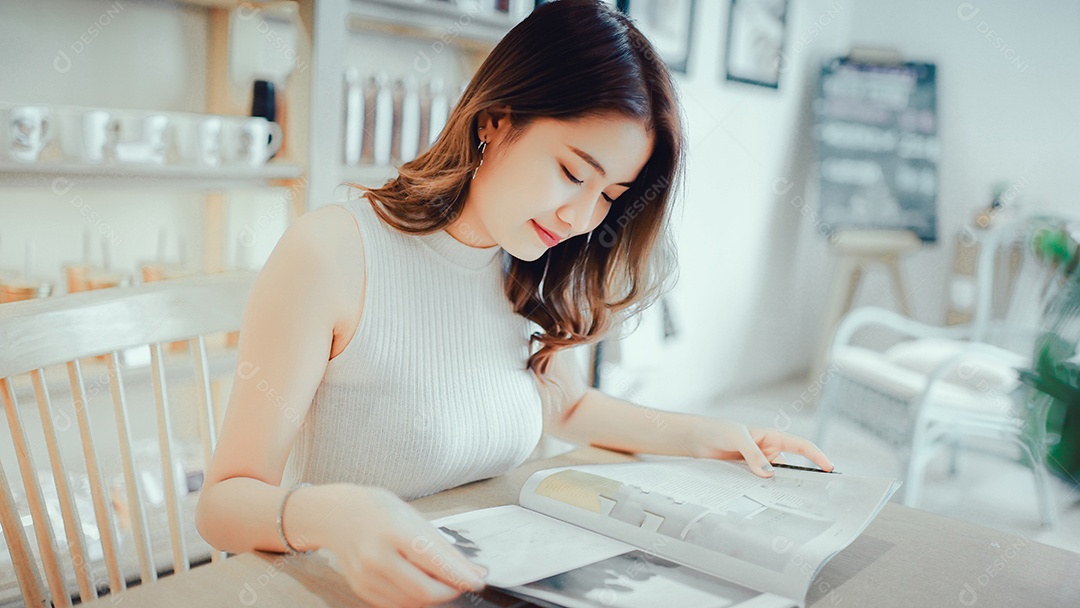 Menina asiática lendo livro de moda sorria na cafeteria