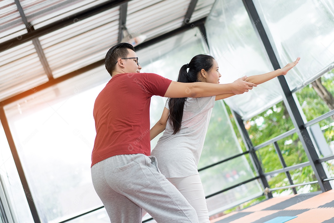 Treinador pessoal treinando com jovem asiática em aula de exercícios de ioga