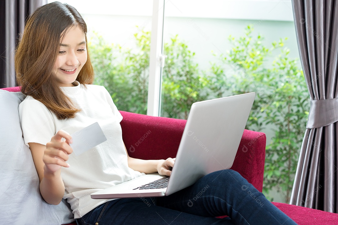 Jovem asiática segurando cartão com laptop para pagamento de compras on-line