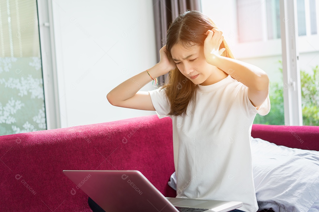 Menina asiática trabalhando em computador tampando os ouvidos