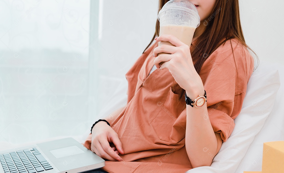 Mulher bebendo café frio e usando computador portátil em casa