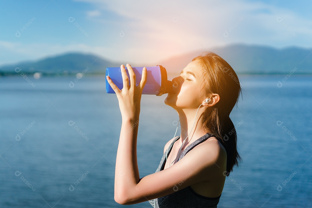 Jovem asiática bebendo shake de proteína com sutiã esportivo após exercícios ao ar livre