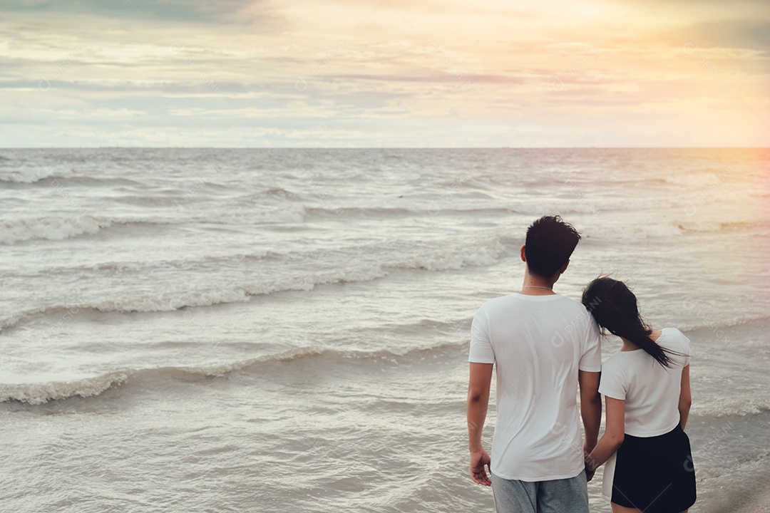 Jovem asiático de mãos dadas com a garota romântica juntos na praia