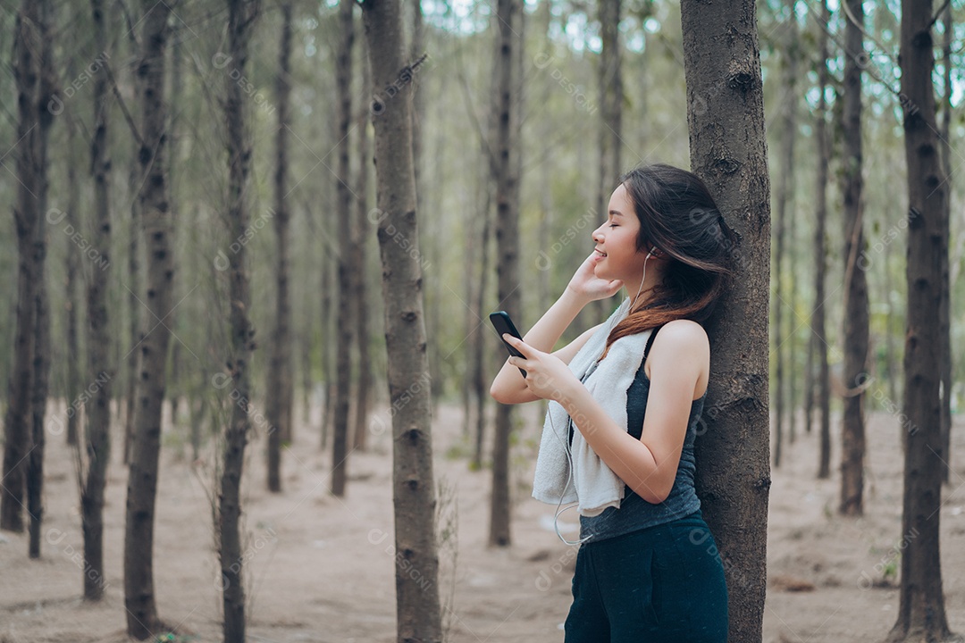 Mulher asiática ouvindo música na floresta depois do treino do corredor