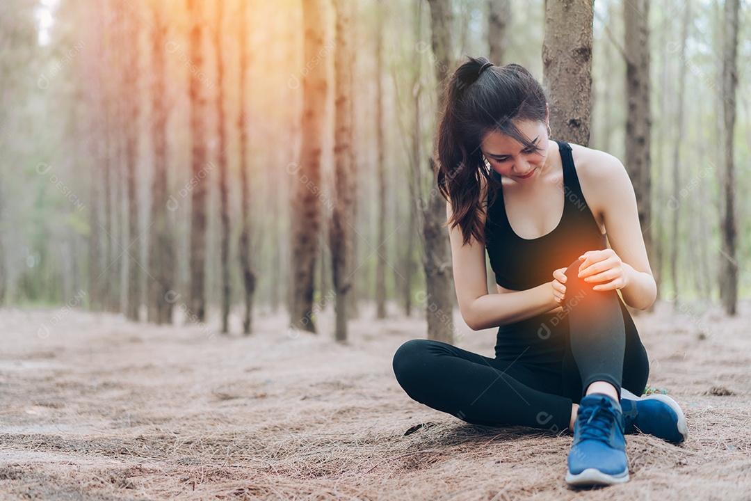 Mulher jovem com dor no joelho pós corrida na floresta