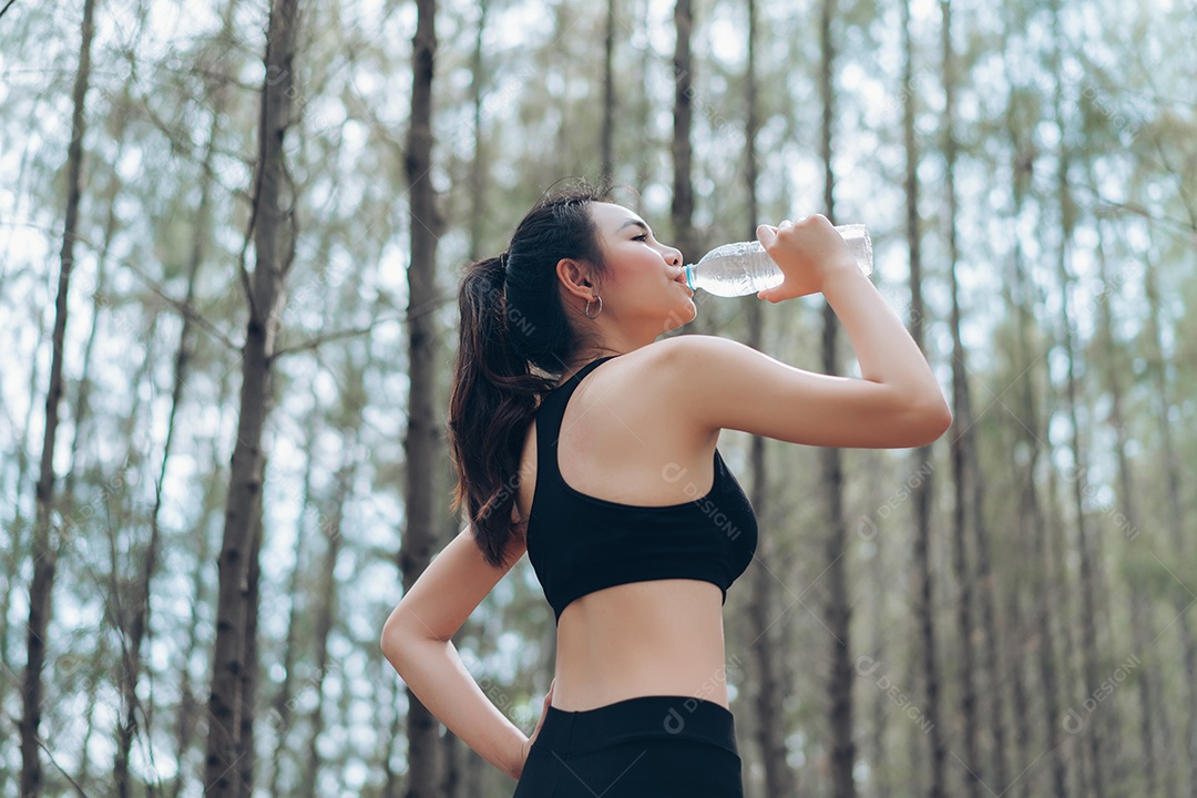 Jovem mulher se hidratando em exercícios na floresta