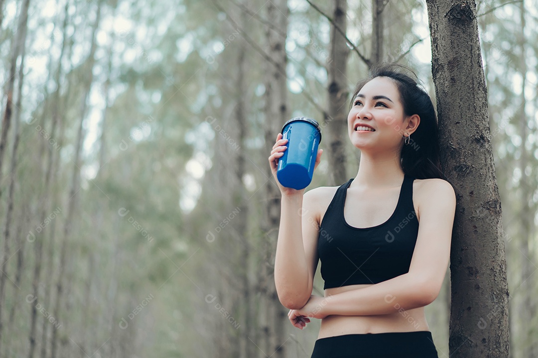 Linda mulher asiática bebendo garrafa de água fresca na natureza da floresta para relaxar após o exercício