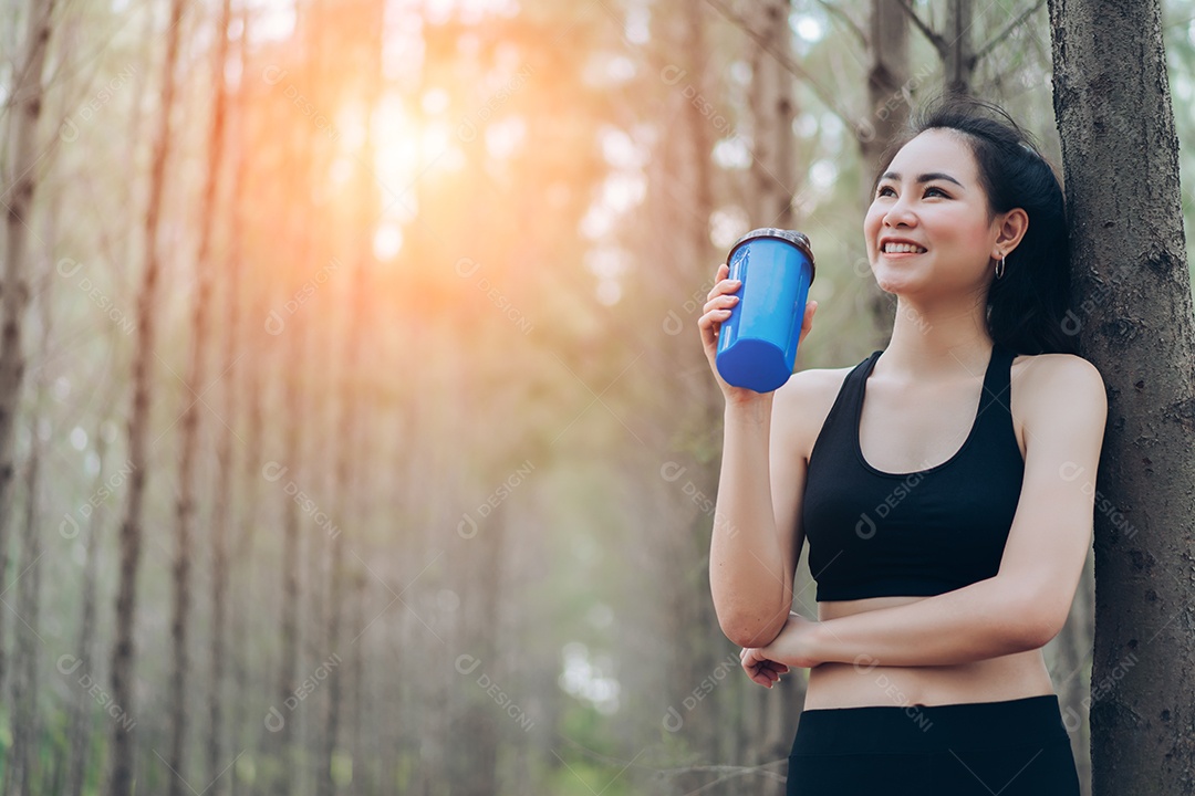 Linda mulher asiática bebendo shake de proteína na natureza da floresta para relaxar após treino cardio