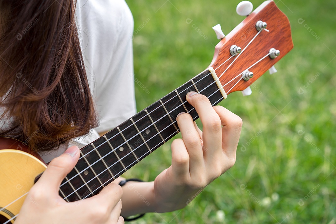 Jovem mulher tocando violão sentada no gramado