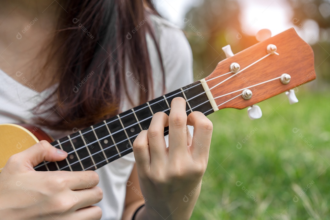 Jovem mulher tocando violão sentada no gramado