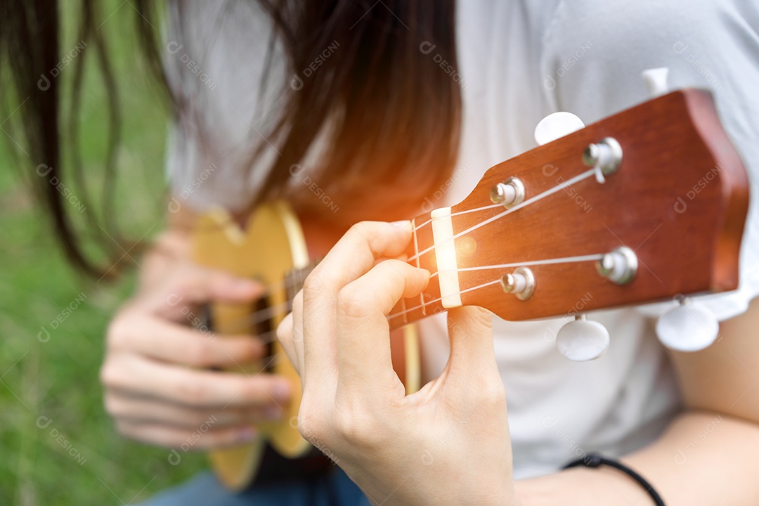 Jovem mulher tocando violão sentada no gramado