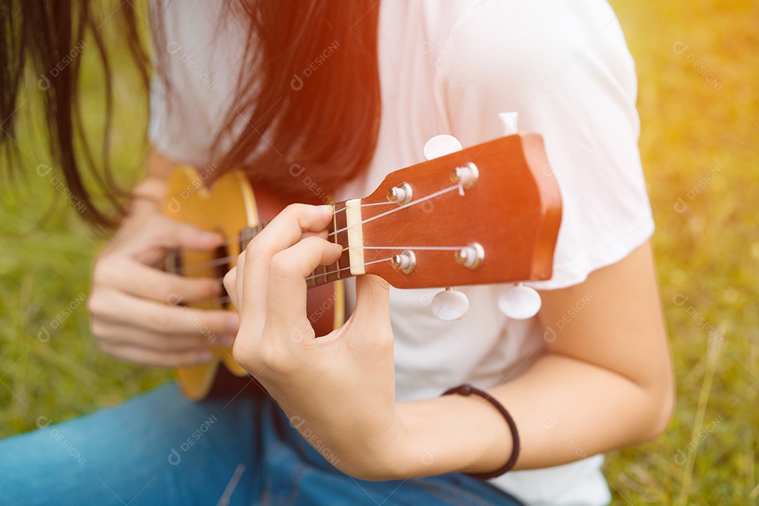 Jovem mulher tocando violão sentada no gramado