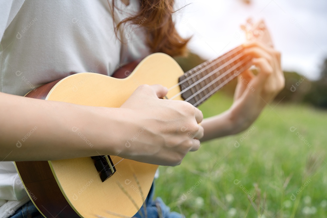 Jovem mulher tocando violão sentada no gramado