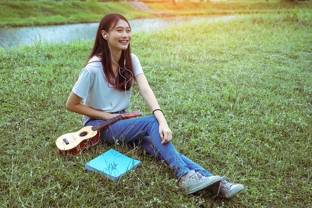 Jovem mulher tocando violão sentada no gramado