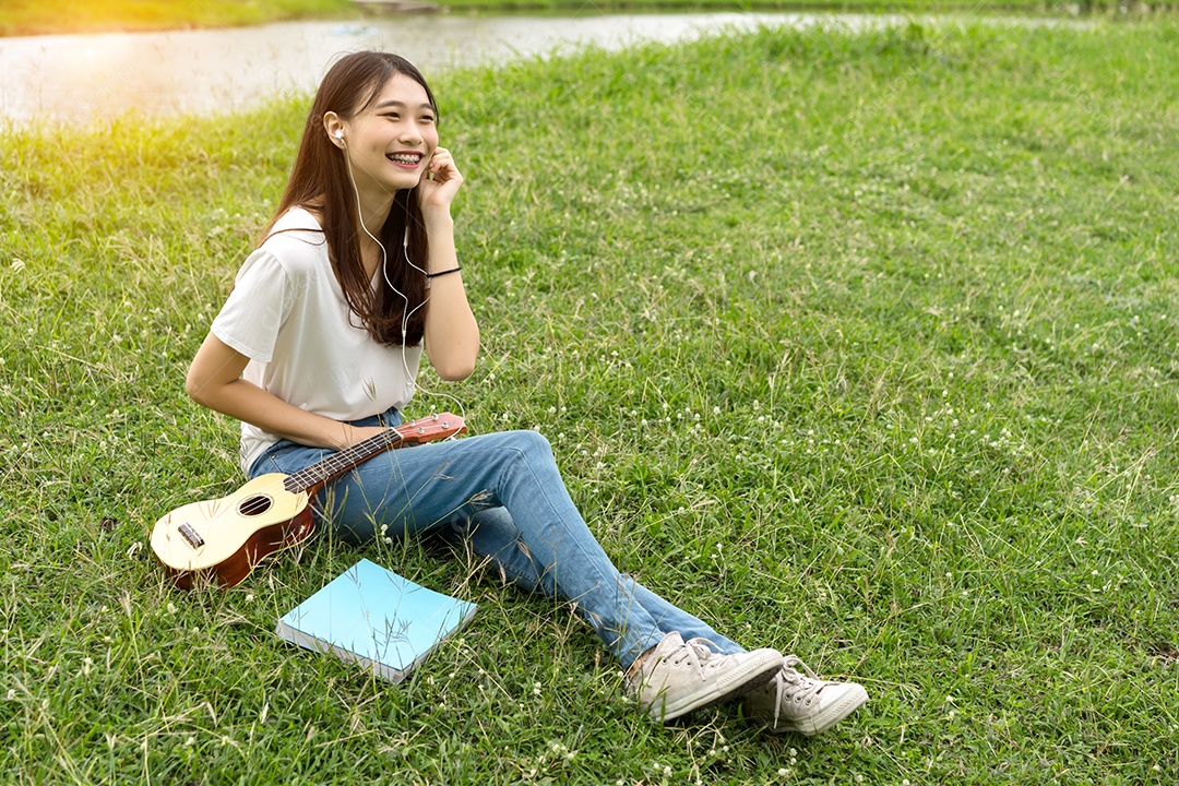 Jovem mulher tocando violão sentada no gramado