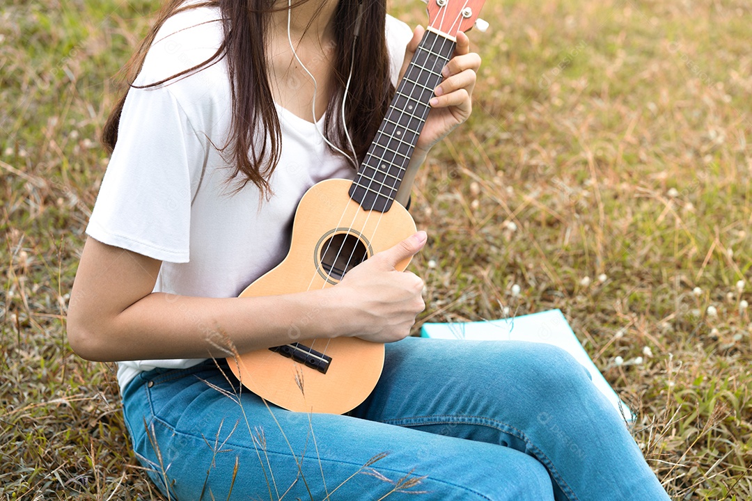 Jovem mulher tocando violão sentada no gramado