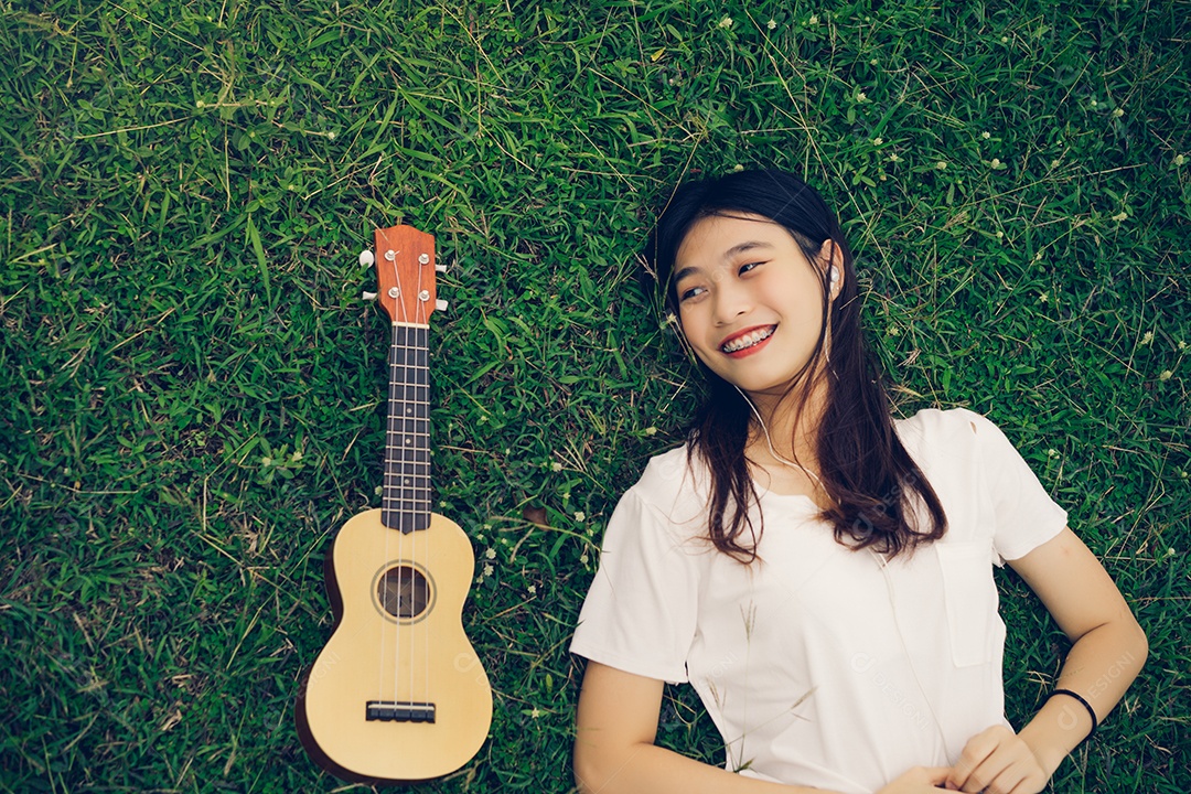 Jovem mulher tocando violão sentada no gramado