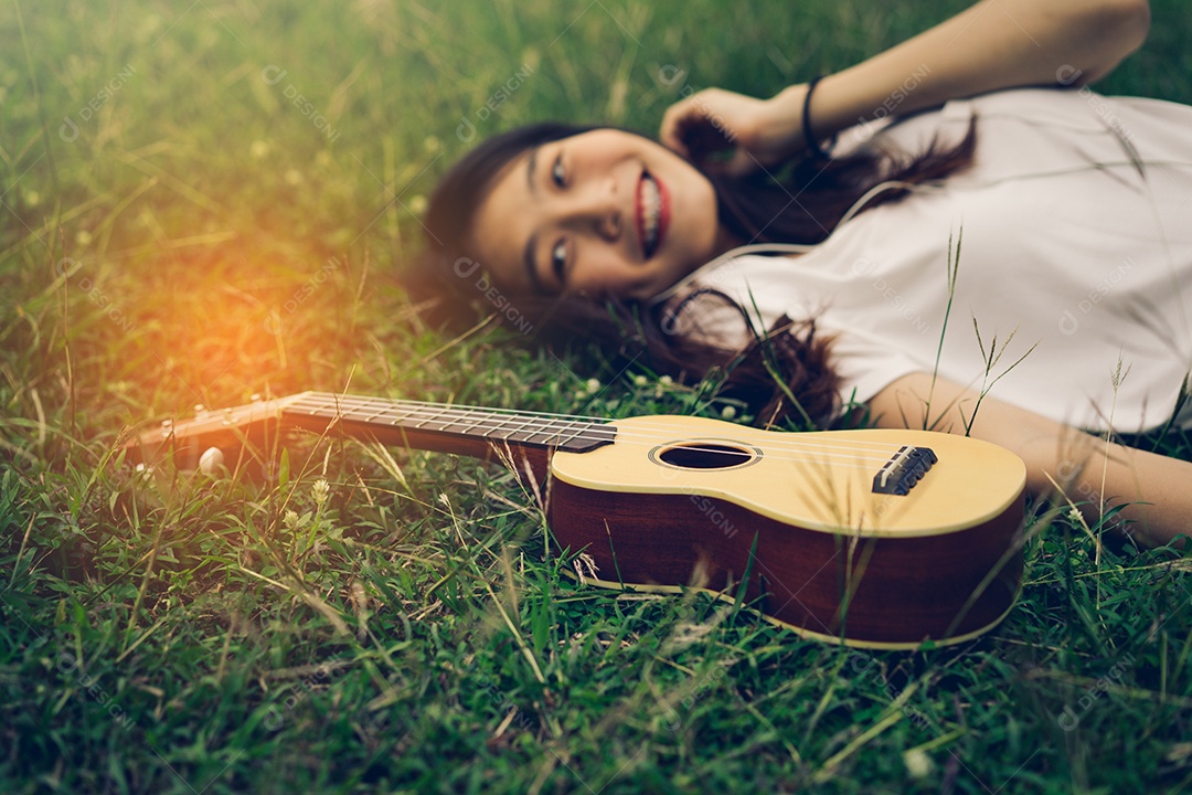Jovem mulher tocando violão sentada no gramado