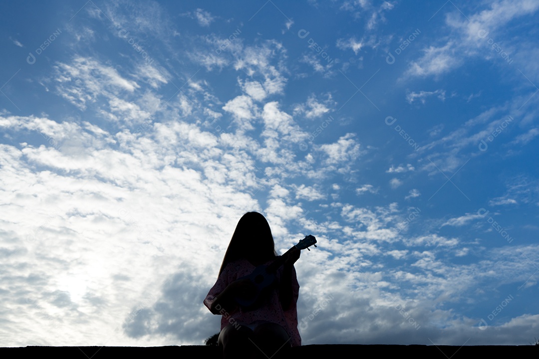 Mulher tocando ukulele contra céu azul