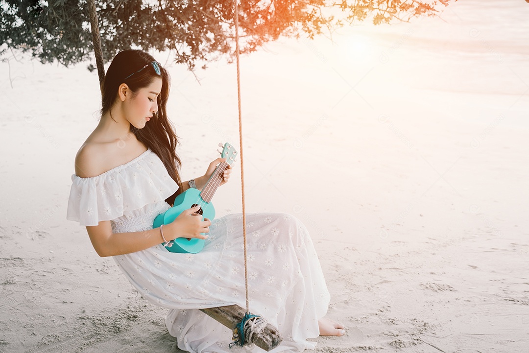 Mulher asiática solitária tocando ukulele sentada no balanço na praia